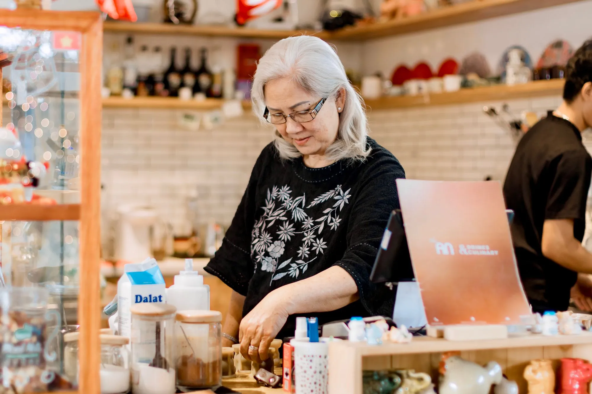 A shopkeeper working behind the counter of a small, well-stocked shop