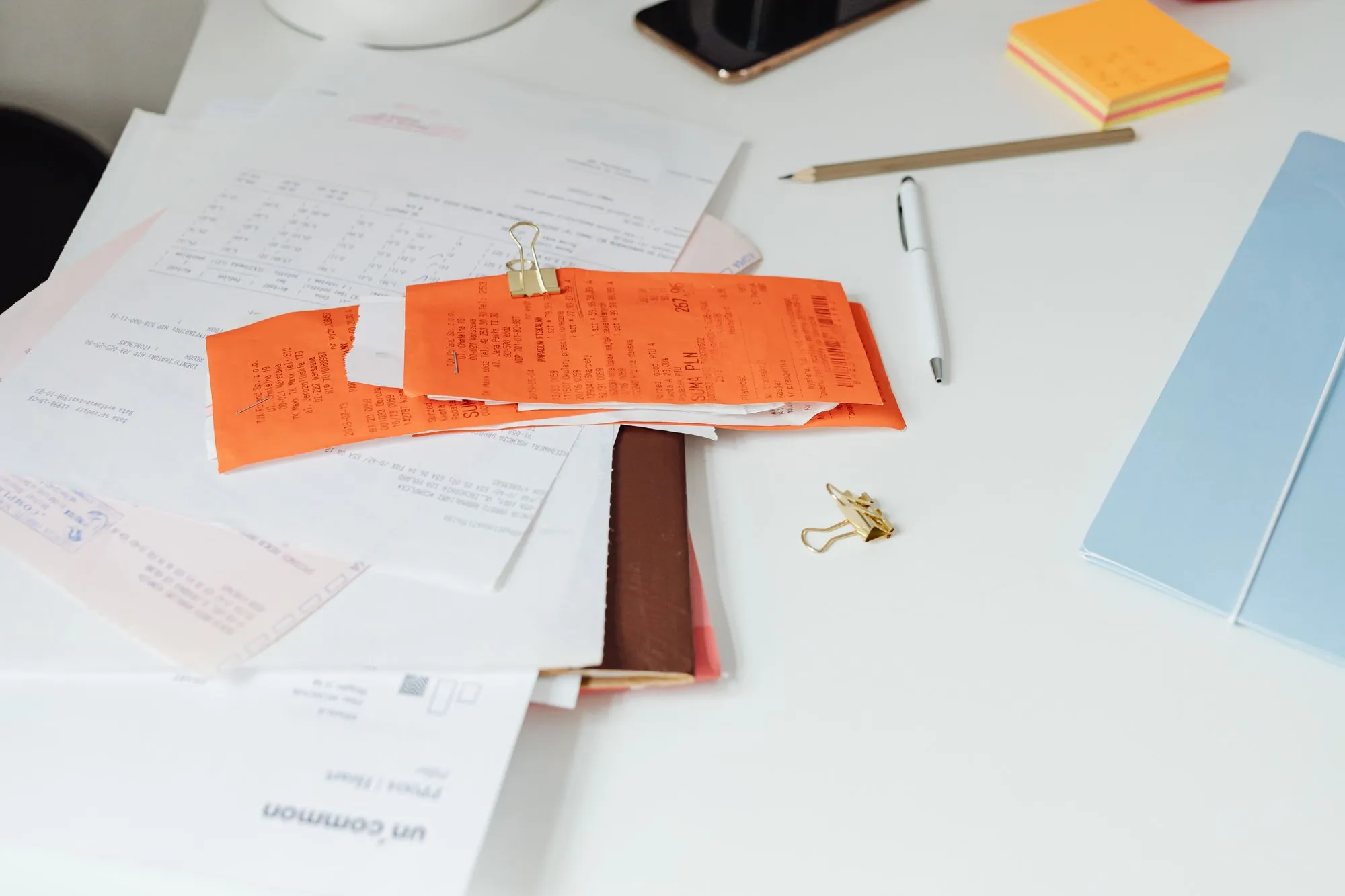 Paper receipts and invoices scattered across a desk beside a pen and notepad